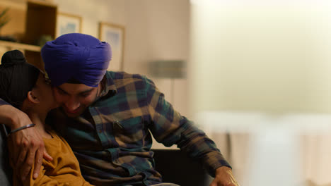 Loving-Sikh-Father-And-Son-Wearing-Turbans-Sitting-On-Sofa-At-Home-Talking-Together